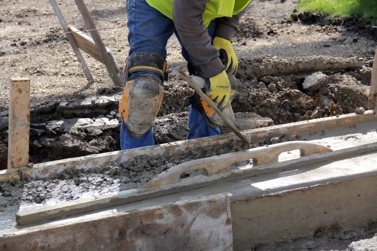Worker smoothing freshly placed concrete with a hand trowel